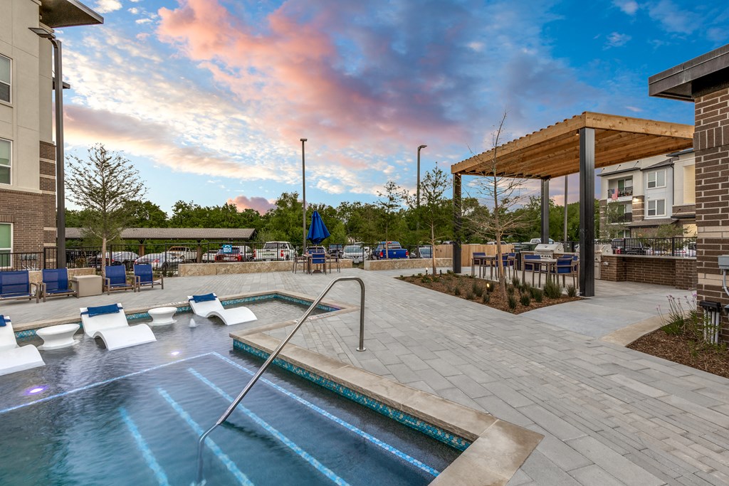 an outdoor pool with lounge chairs and a spa at a apartment complex