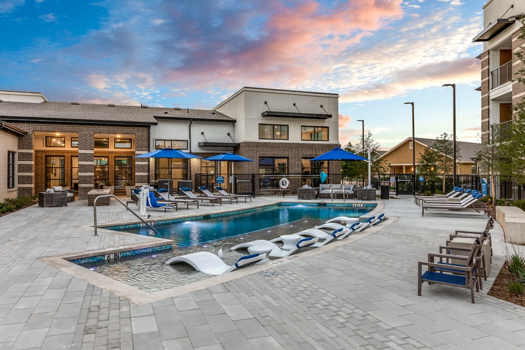 a resort style pool with lounge chairs and umbrellas in front of a building