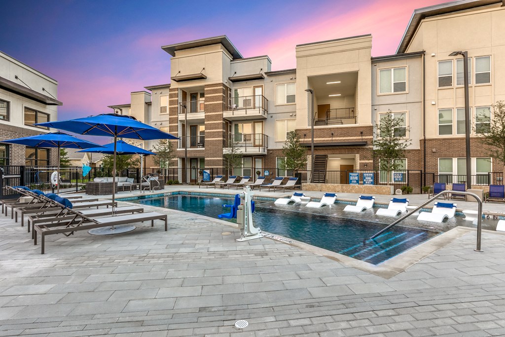 a swimming pool with lounge chairs and umbrellas in front of an apartment building
