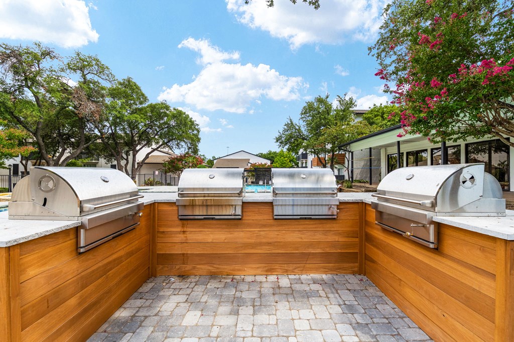 two bbq grills in the backyard of a home with a pool in the background