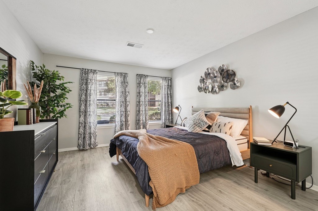 A bedroom with a bed, nightstand, and a plant.