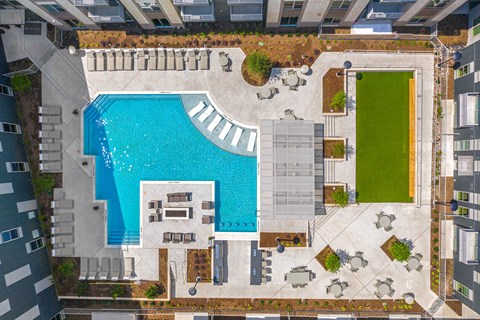 A large swimming pool surrounded by a patio area with chairs and a small grassy area.
