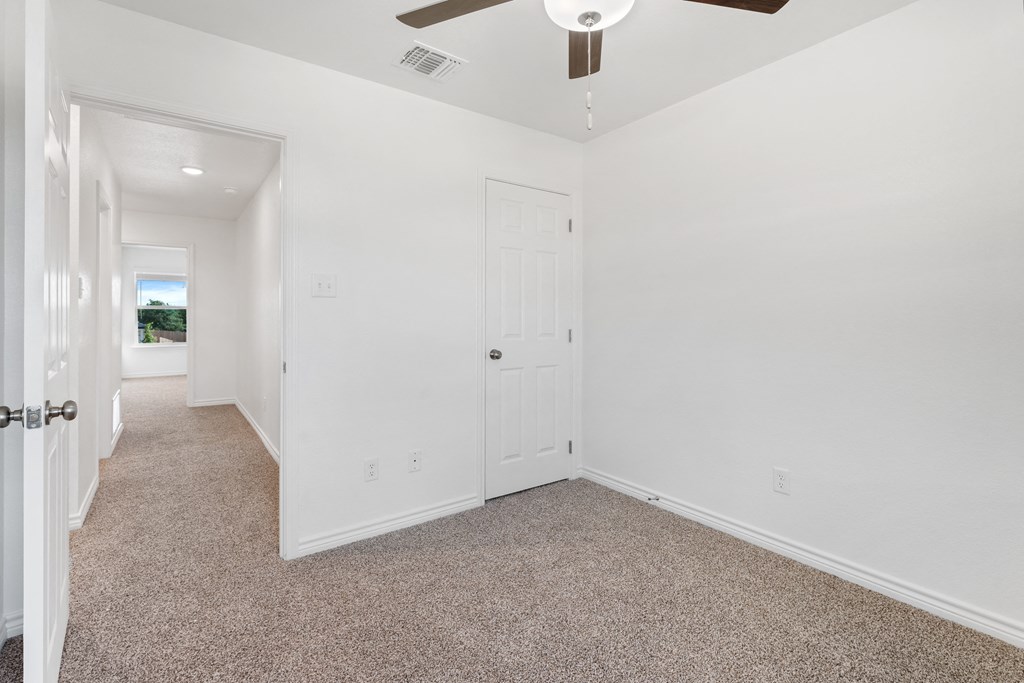 an empty room with white walls and carpet and a ceiling fan