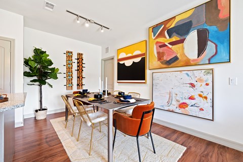 A dining room with a table and chairs and a painting on the wall.