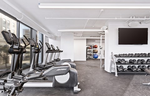 a gym with various cardio machines and a television