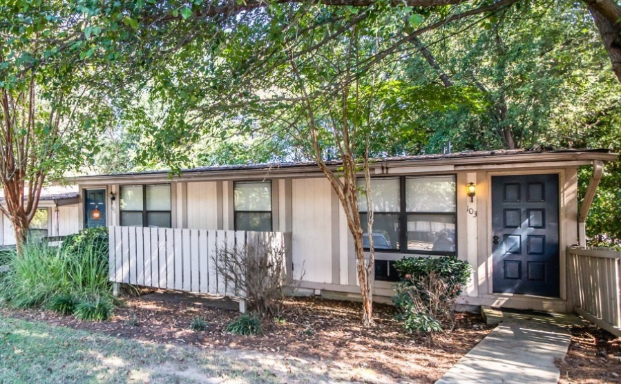 a small house with a white fence and trees in front of it