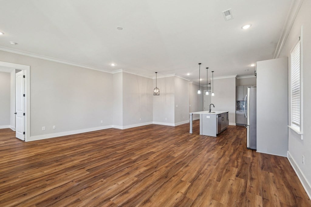 A large empty room with wooden floors and a kitchenette in the corner.