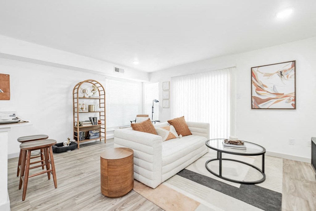 A living room with a white couch, a wooden chair, and a glass coffee table.