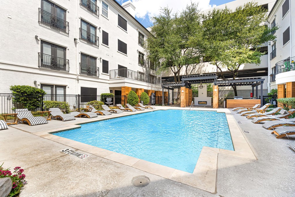 an outdoor pool with lounge chairs and trees in front of an apartment building