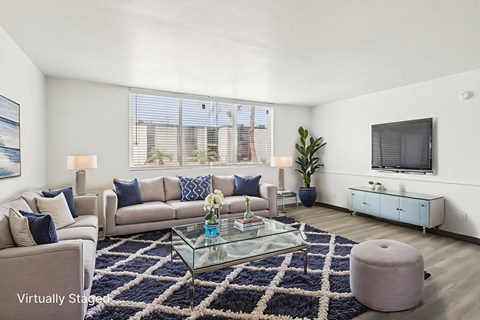 A living room with a glass coffee table and a large window.