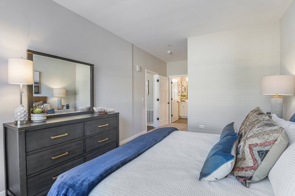 A bedroom with a large bed and a dresser with a mirror above it.