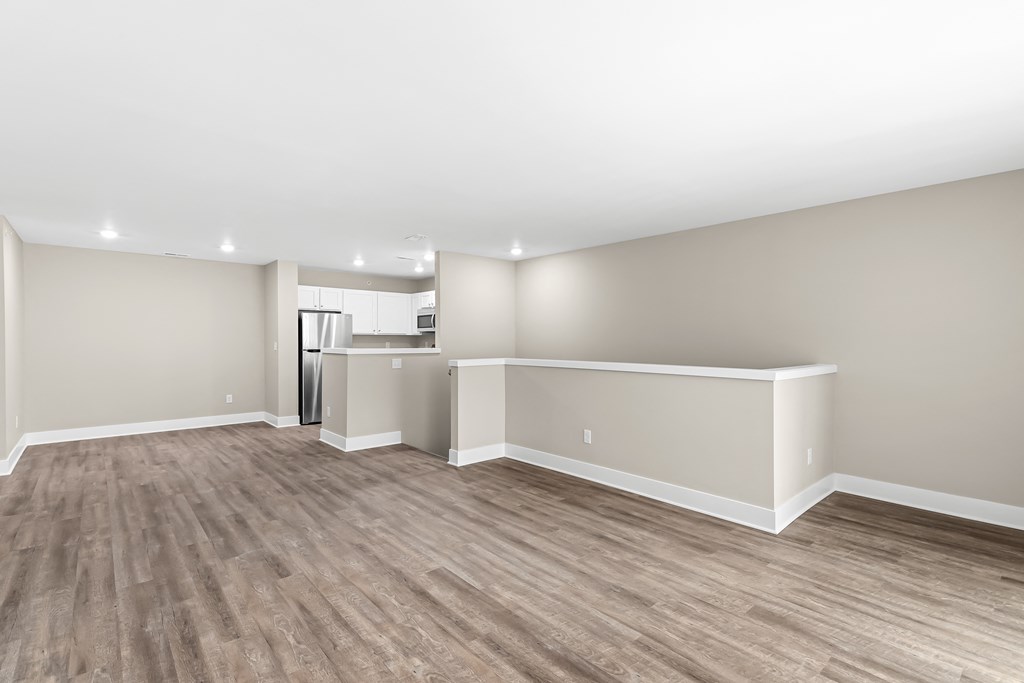 an empty living room with wood flooring and a kitchen