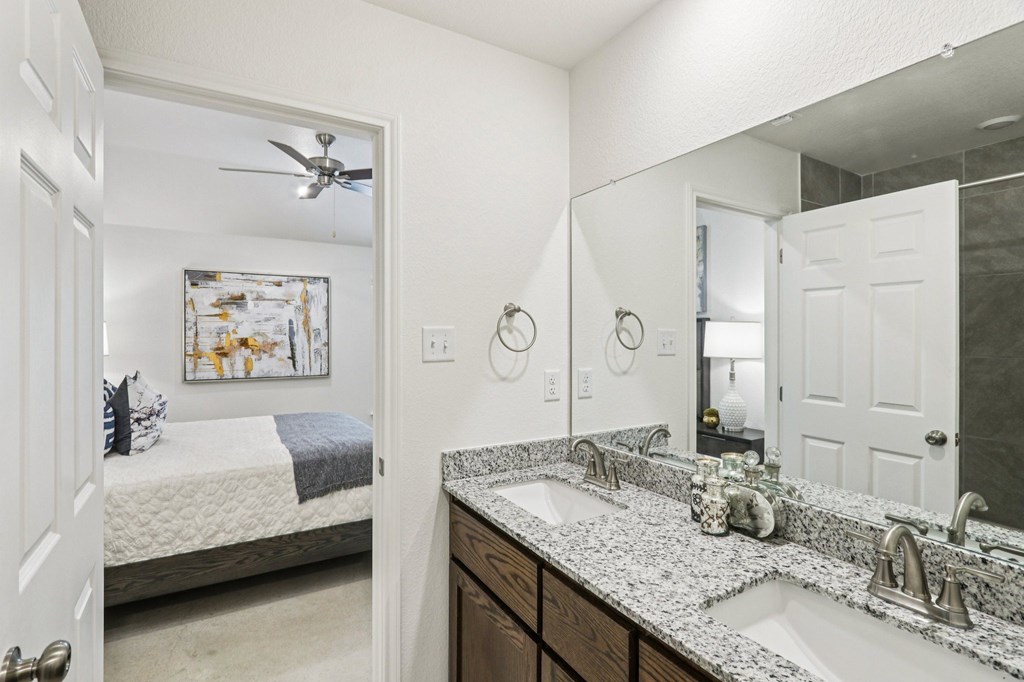 A bathroom with a bed in the background and a mirror above the sink.