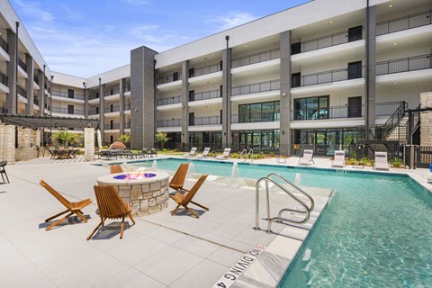 a swimming pool with chairs and a fire pit in front of a hotel