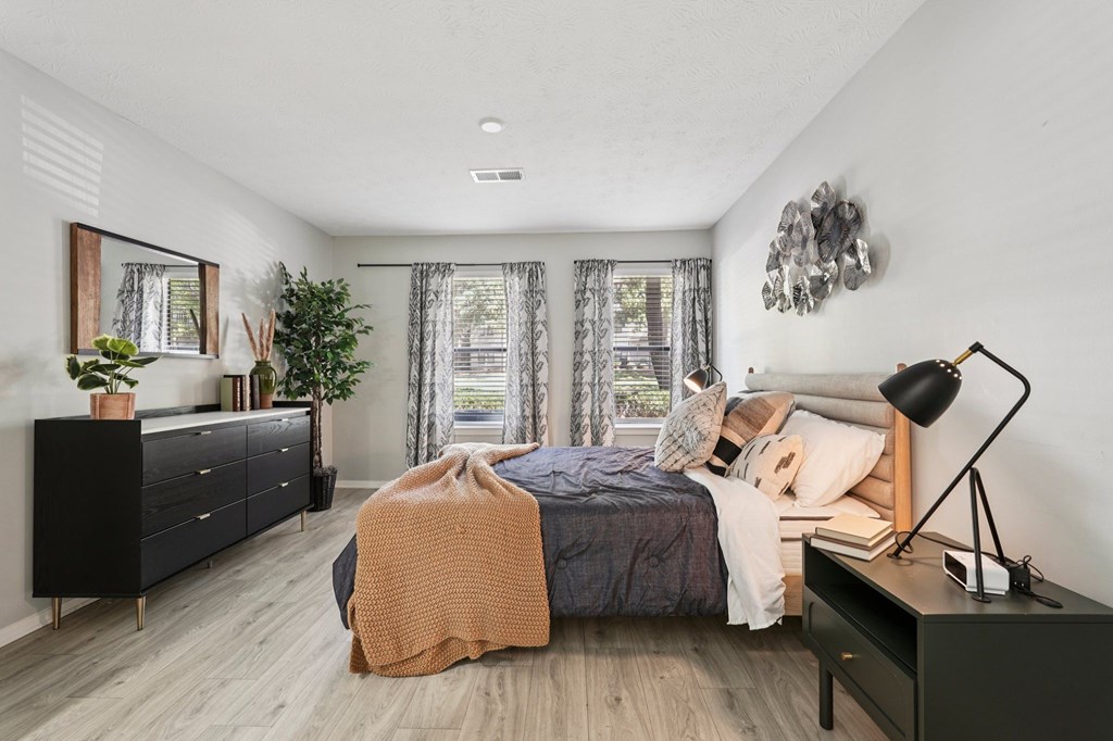 A bedroom with a bed, nightstand, and a plant.