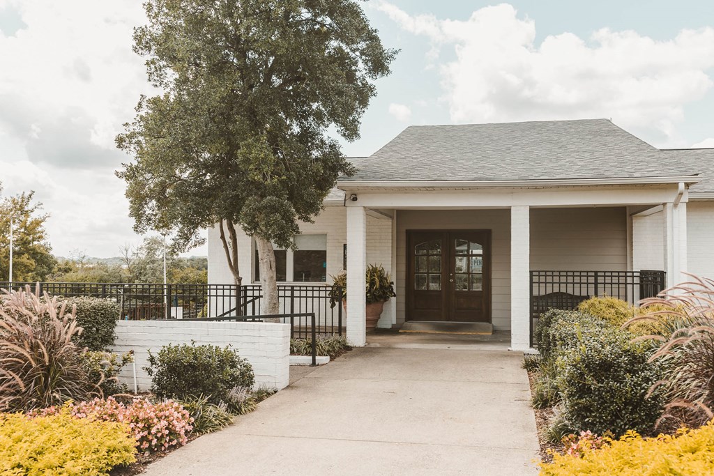 the front of a white house with a sidewalk and a tree