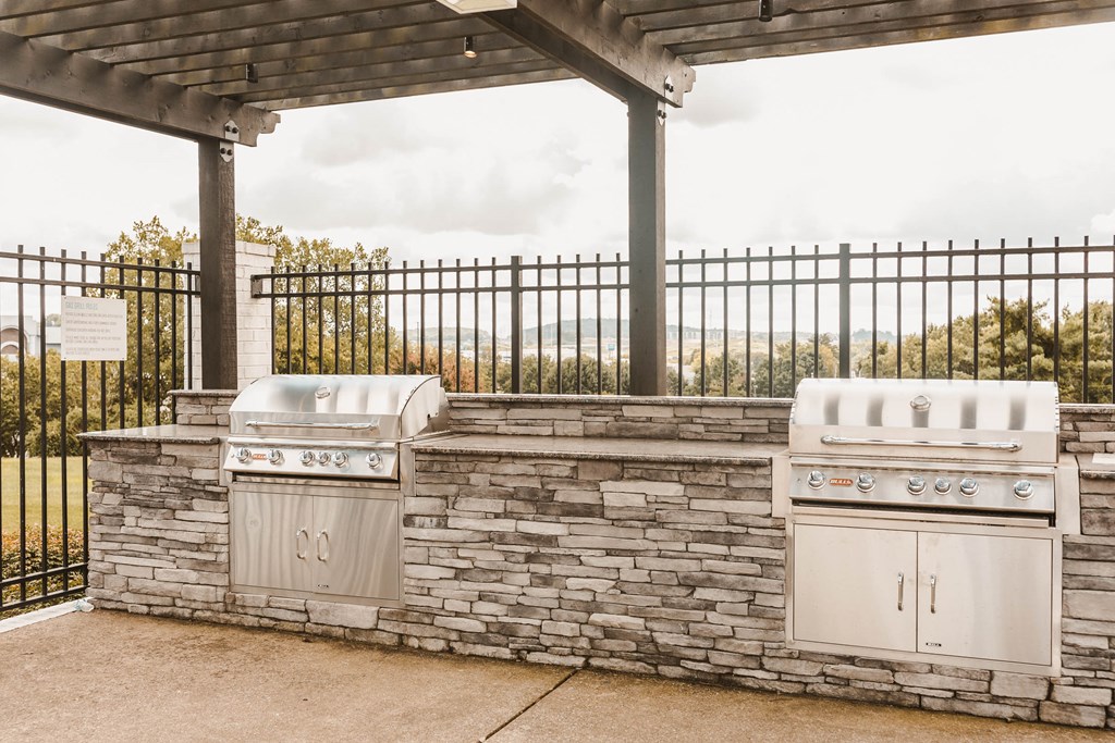 two outdoor barbecue grills next to a stone wall with a pavilion