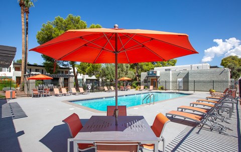 A red umbrella shades a table by a pool.