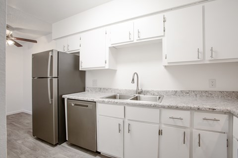 A kitchen with a refrigerator, sink, and cabinets.