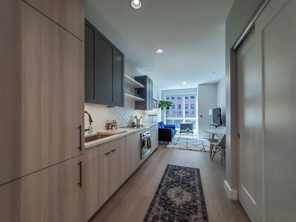 A modern kitchen with wooden cabinets and a blue rug on the floor.
