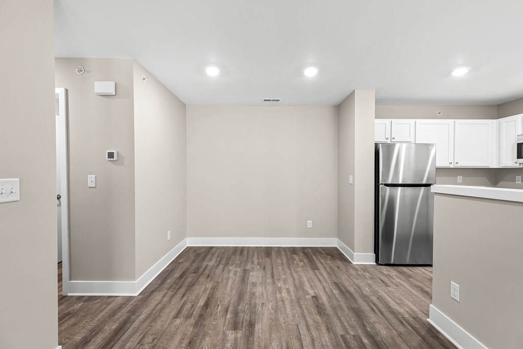 an empty living room with a kitchen and a stainless steel refrigerator