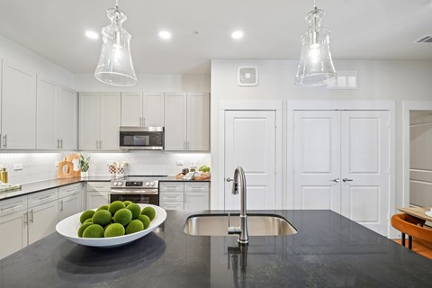 A modern kitchen with a black countertop and a bowl of green fruit on it.