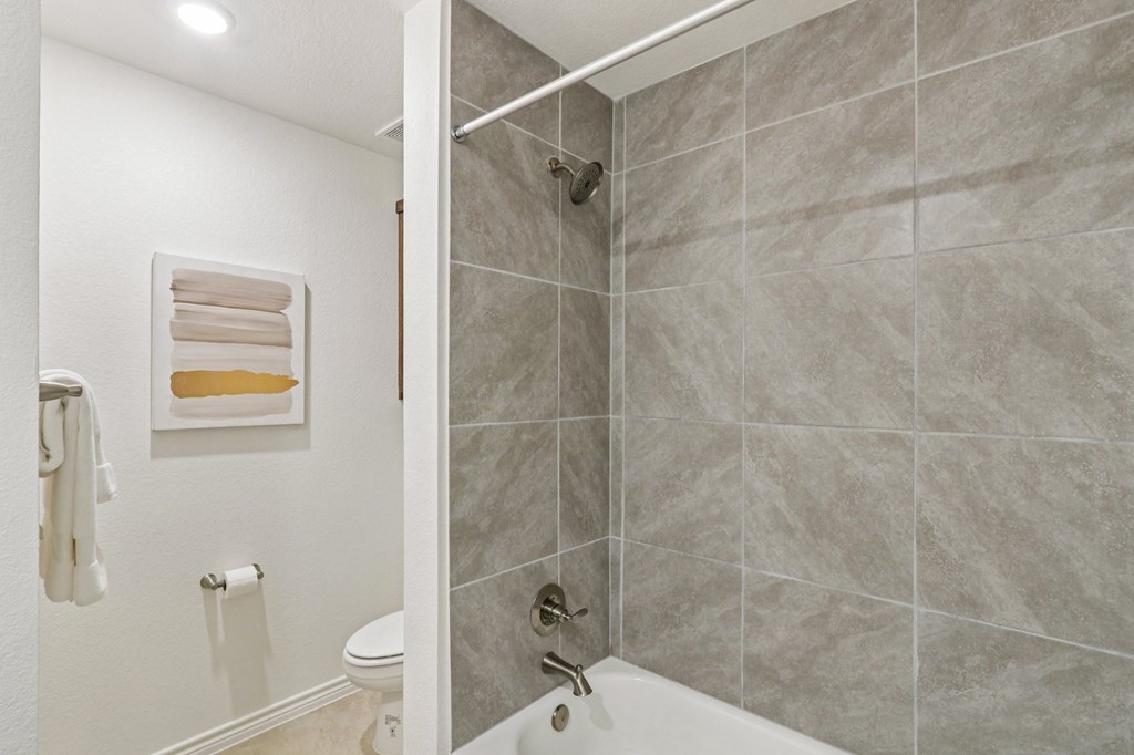 A bathroom with a toilet, a shower, and a towel hanging on the wall.