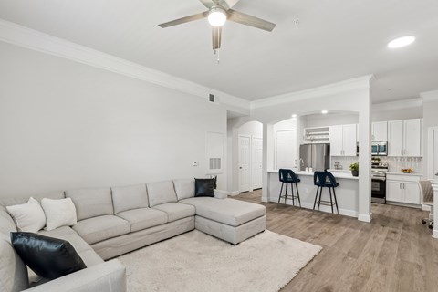 A living room with a grey couch and a white ceiling fan.