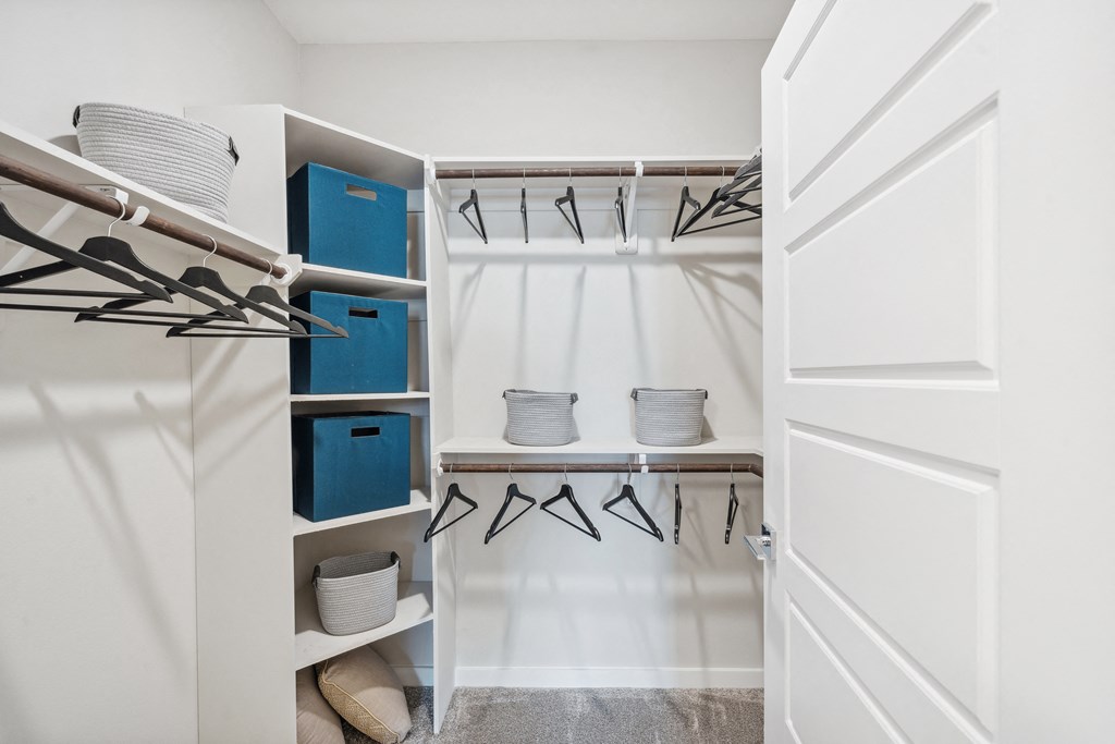 a walk in closet with white walls and a white closet door with baskets and chairs
