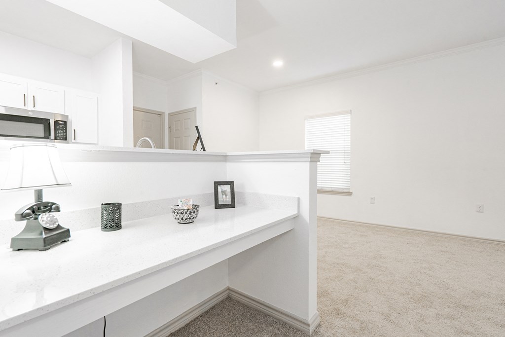 a white kitchen with a white counter top and a microwave and a window