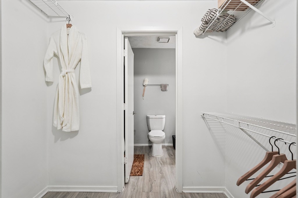 A white bathroom with a toilet and a white robe hanging on the wall.
