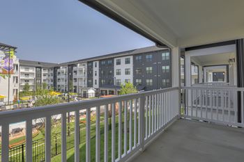 A balcony with white railings overlooks a grassy area and apartment buildings.