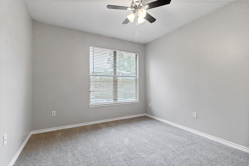 an empty bedroom with a ceiling fan and a window