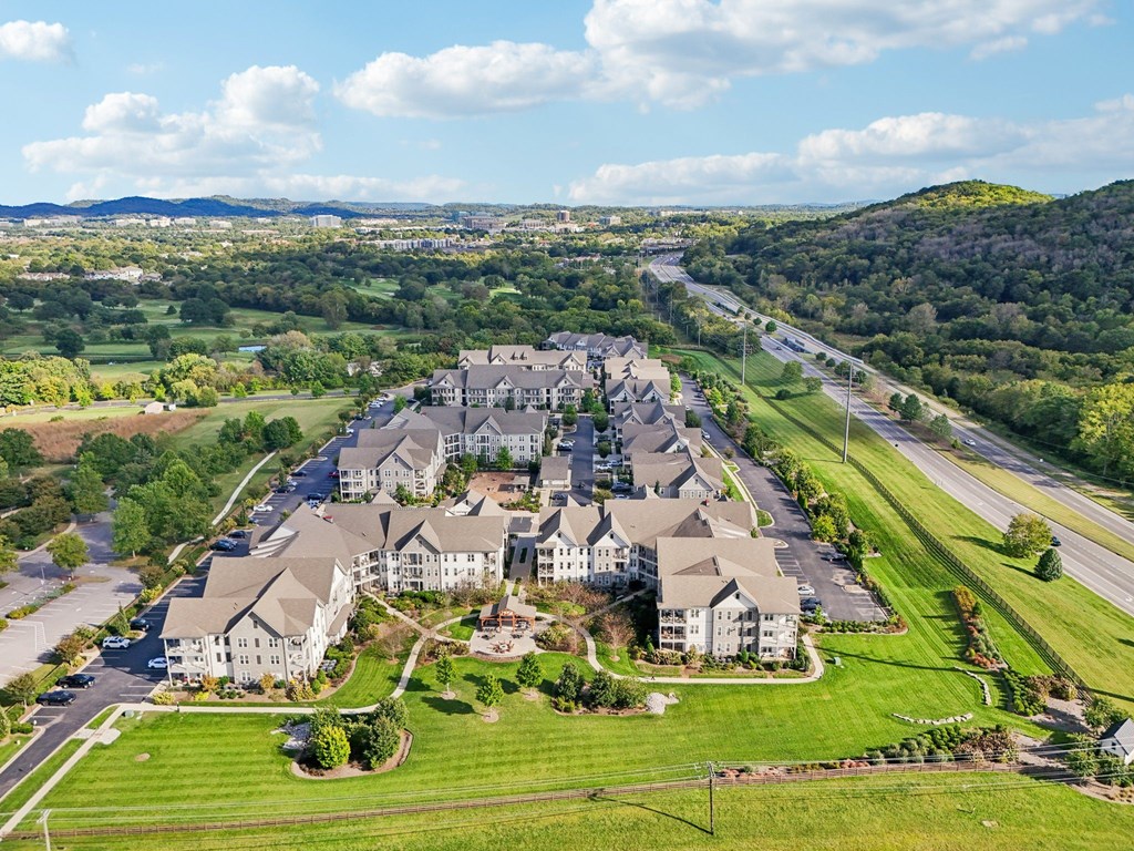 A large, multi-story building with a parking lot in front is surrounded by greenery.