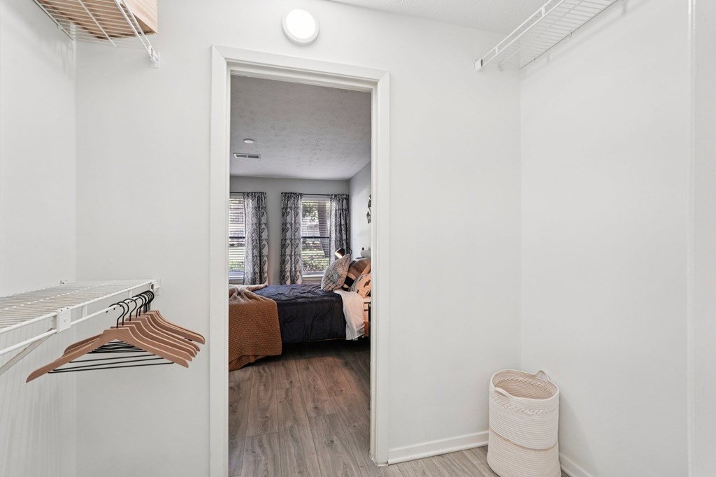 A bedroom with a bed, a window with curtains, and a wardrobe with clothes hanging on it.