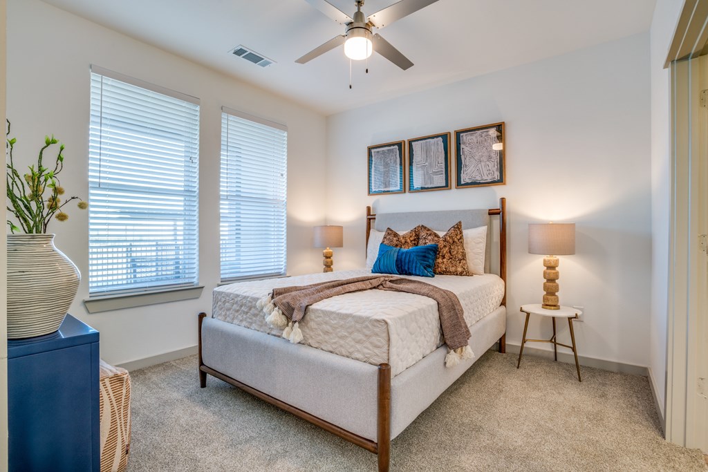 A bedroom with a bed, a ceiling fan, and a window with blinds.