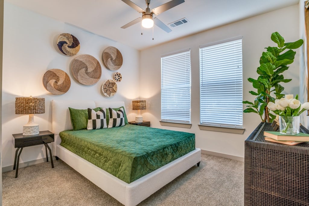 A bedroom with a bed, a fan, and a plant.