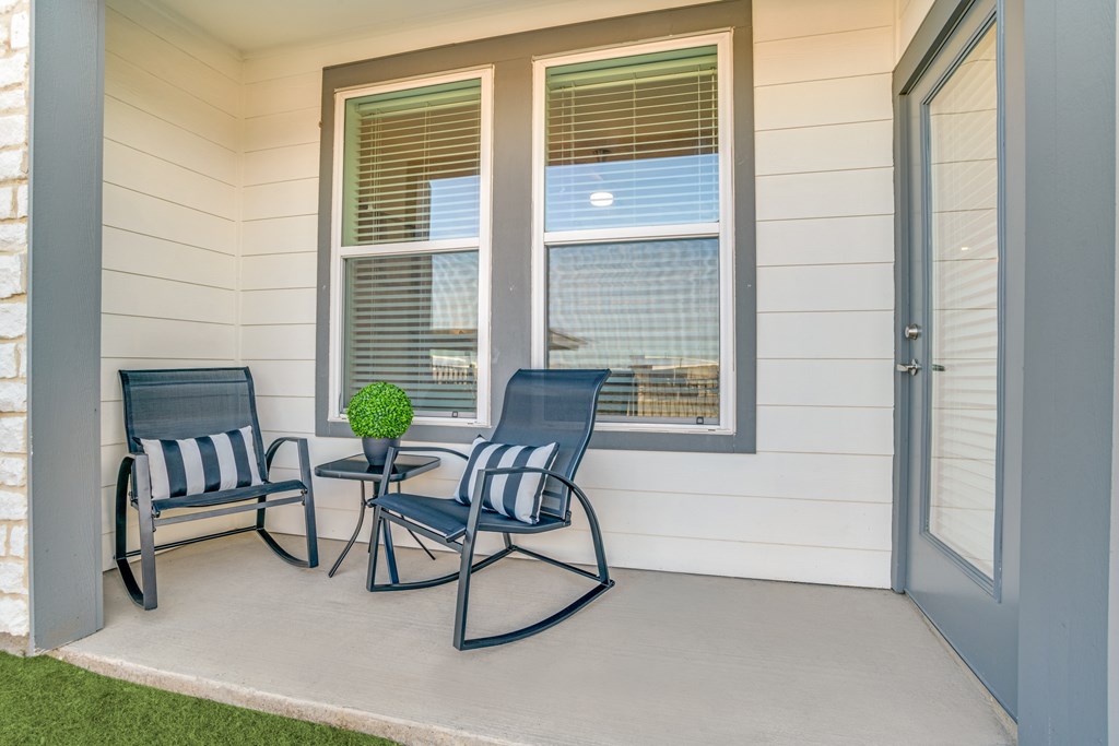 A small table with a plant on it sits between two chairs on a porch.