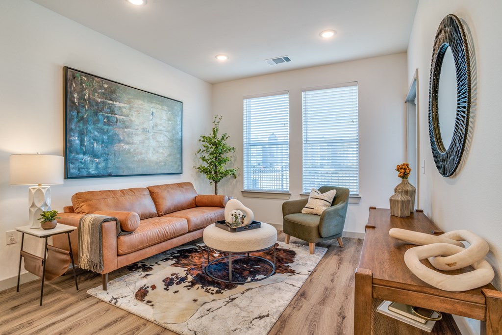 A living room with a brown leather couch, a white coffee table, and a large painting on the wall.