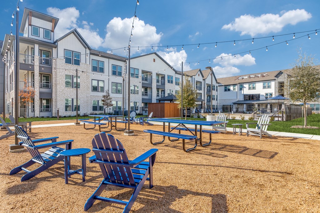 a playground with blue chairs and picnic tables in front of an apartment building