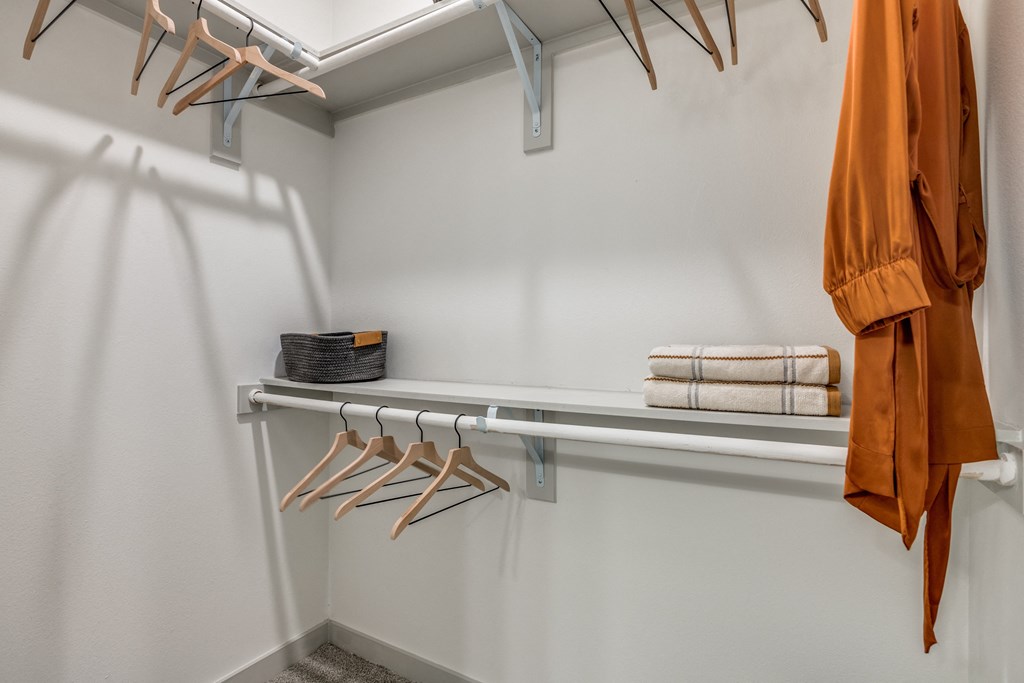 a walk in closet with a white wall and a rack with hangers and towels