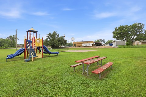 A playground with a yellow and blue slide, a red and white picnic table, and a green lawn.