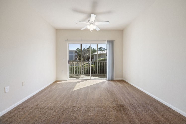 an empty living room with a ceiling fan and a balcony