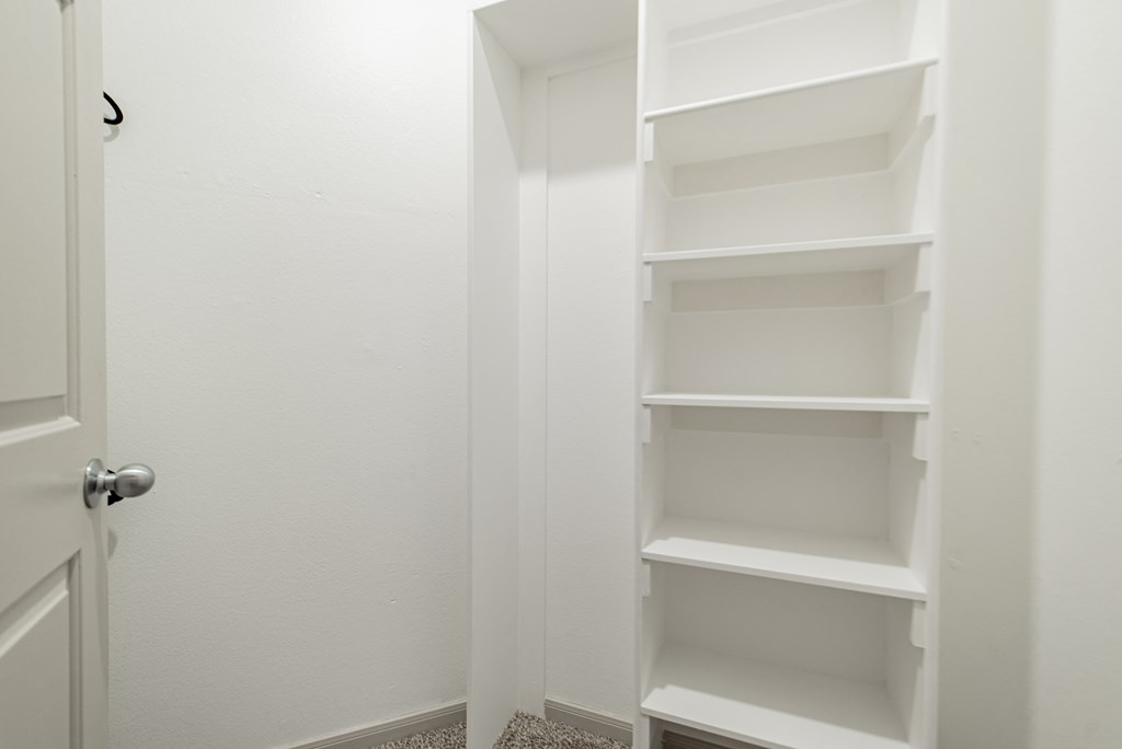 an empty closet in a bathroom with white shelves