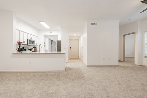 an empty living room with a kitchen and a door to a hallway