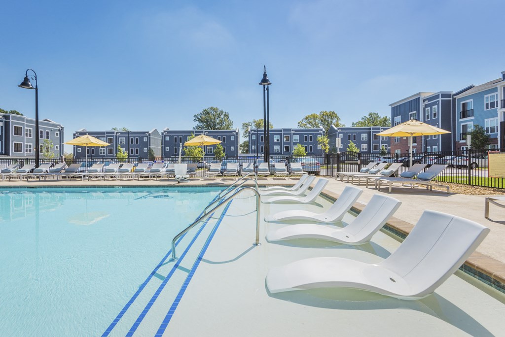A pool with sun loungers and a building in the background.