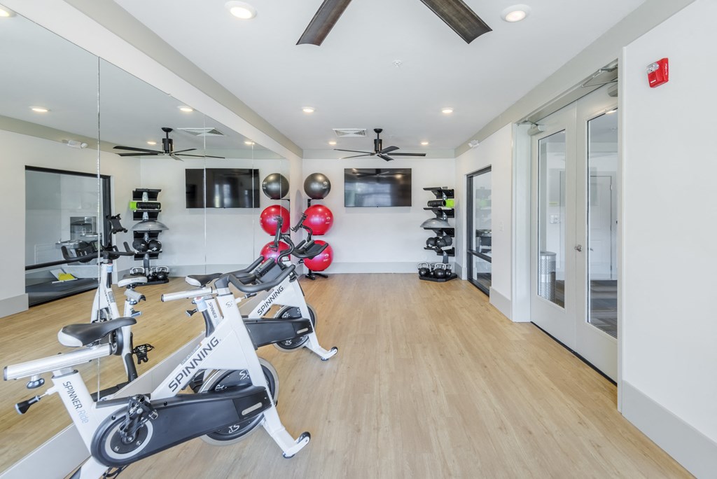 A gym with a row of stationary bikes and a television mounted on the wall.