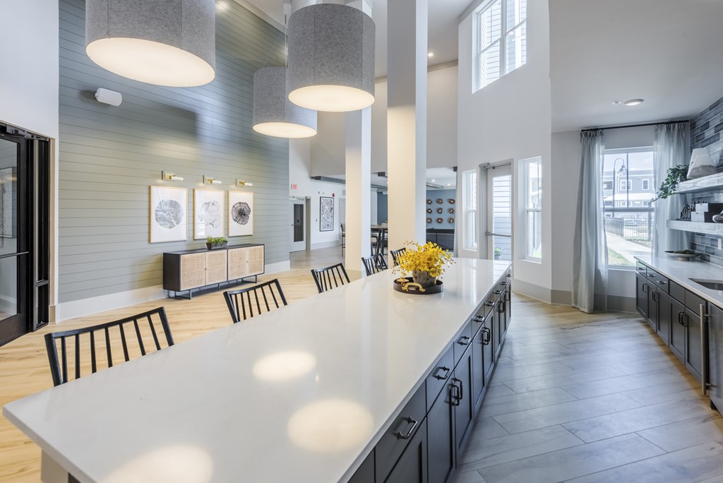 A modern kitchen with a long white island and black chairs.