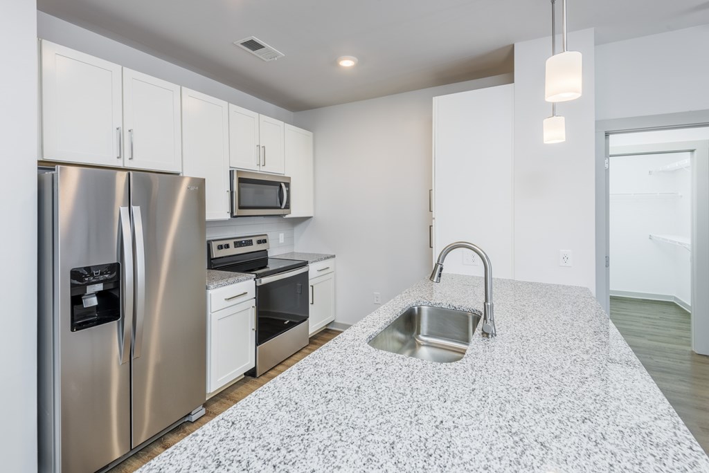 A kitchen with a refrigerator, microwave, oven, and sink.