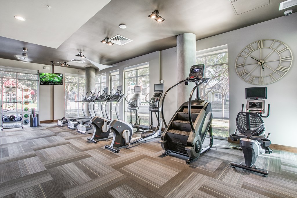 a gym with cardio machines and a large clock on the wall